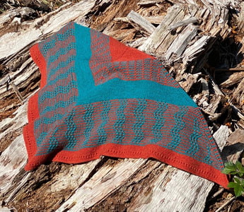 Mosaic knit shawl in teal and orange laying on wooded area